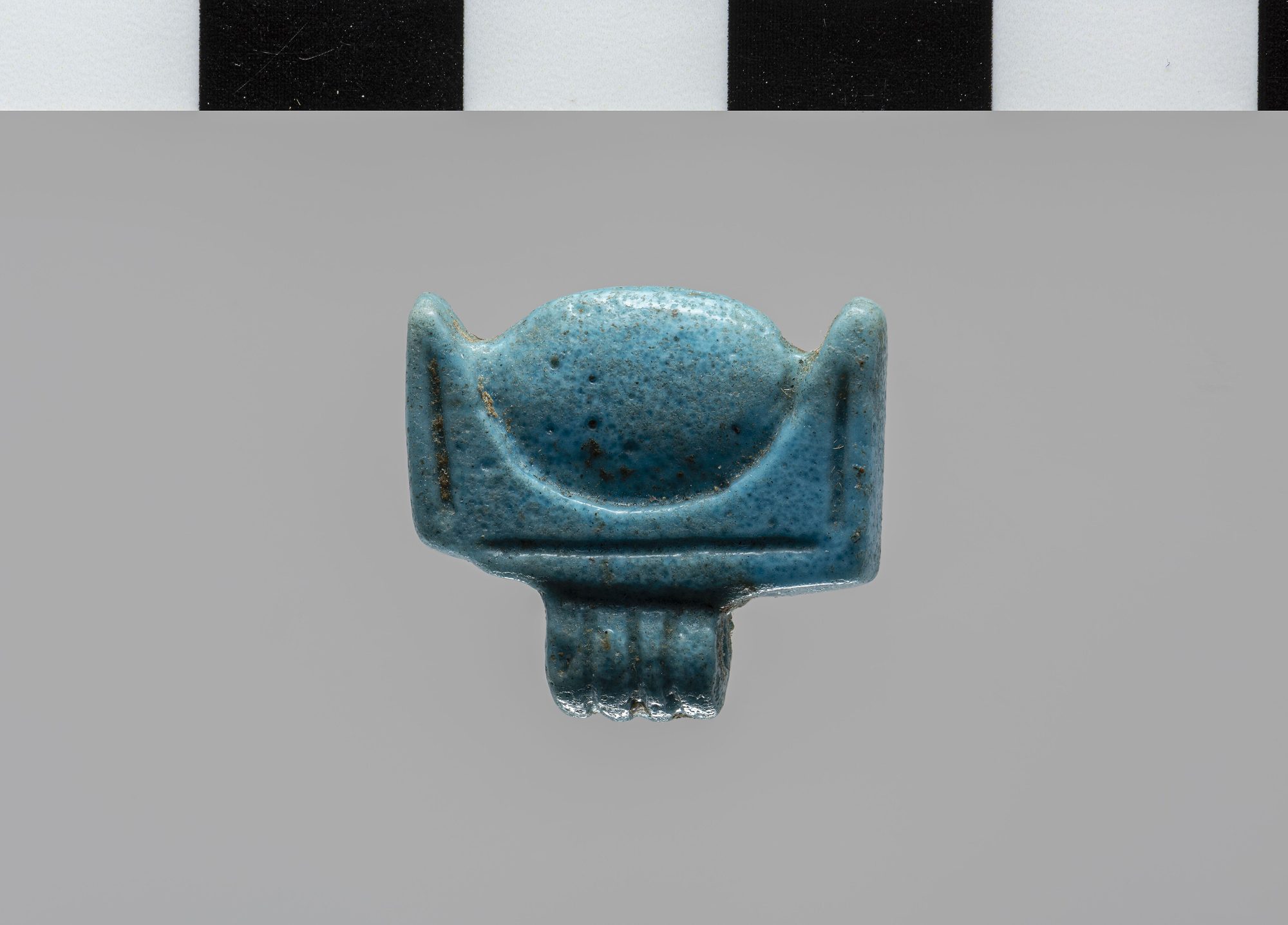 An ancient Egyptian faience amulet in the shape of the akhet — the sun disk cradled between the two hills of the horizon.