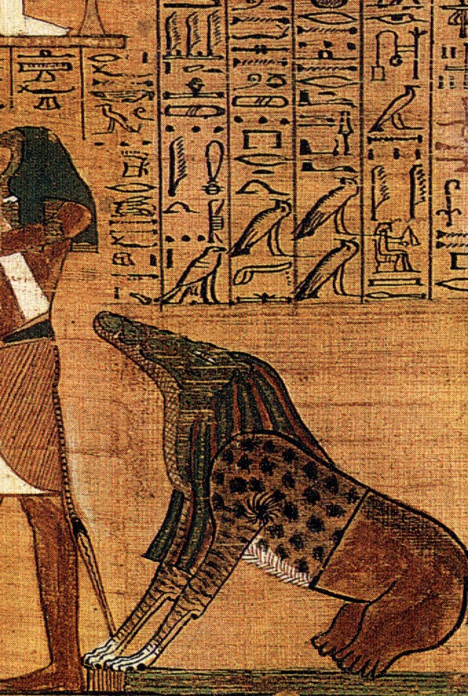Detail from an ancient Egyptian funerary papyrus: the devourer Ammit crouched on the ground beside the judgment scene — a composite beast with the open-jawed head and scaly neck of a crocodile, the spotted-leopard mane and forequarters of a lion, and the heavy hindquarters of a hippopotamus, her four feet resting on the green ground-line; the ibis-headed scribe-god Thoth stands at left with his palette, and columns of hieroglyphs run along the top.