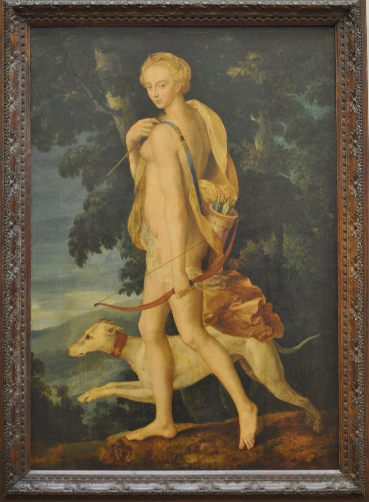 Diana the huntress striding through a dark wood, a gold mantle slipping from her shoulders, reaching back to draw a white-fletched arrow from the quiver at her side while a red recurve bow hangs in her lowered hand. A lean white hound courses at her feet, and a lake glimmers through the trees behind her.