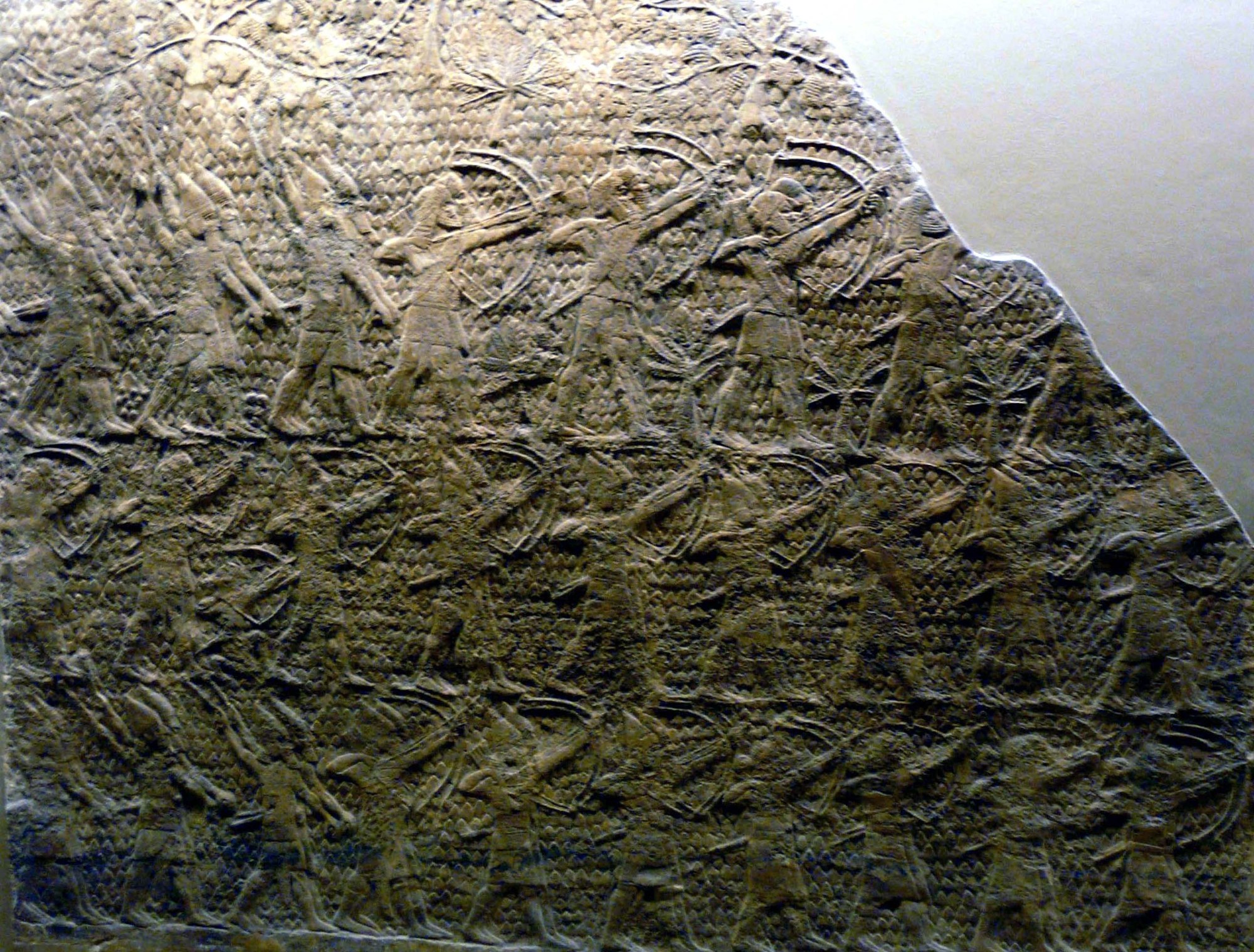 Carved Neo-Assyrian stone relief crowded with soldiers advancing uphill: archers drawing their bows and slingers whirling stones, packed in dense registers across a weathered tan gypsum panel with its broken top edge.