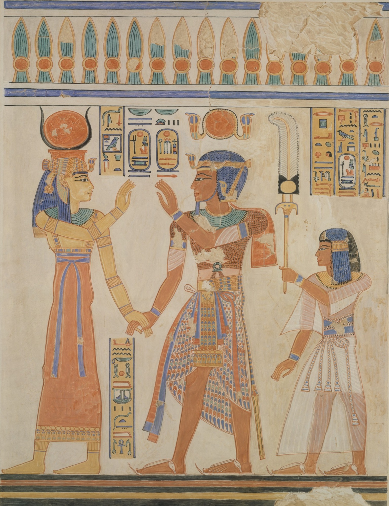 A brightly painted ancient-Egyptian tomb-wall facsimile. At left the goddess Hathor, in a red sheath dress and broad collar, wears the cow-horns-and-sun-disk crown and clasps the king's hand; at centre Ramesses III, in a patterned kilt, beaded corselet and blue headdress, raises one hand toward her; at right the young prince Amenherkhepeshef, in a white pleated robe, holds up a tall feather fan. Columns of hieroglyphs and cartouches fill the field between them, a papyrus-and-lotus frieze runs across the top and a black-and-ochre dado band across the foot, all on a pale plaster ground with the wall's damage-losses recorded.