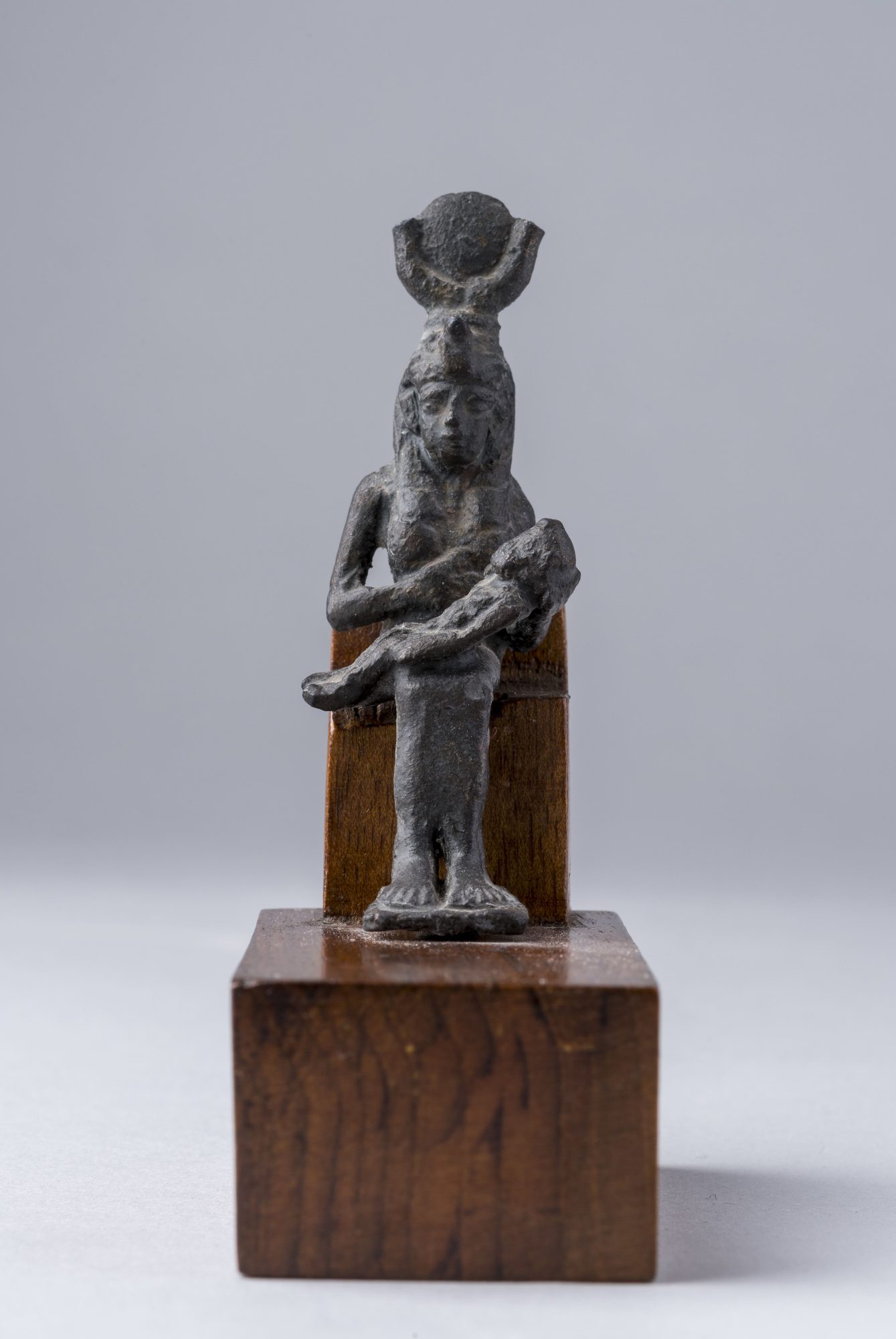 An ancient Egyptian bronze statuette of the enthroned goddess Isis nursing the infant Horus on her lap.