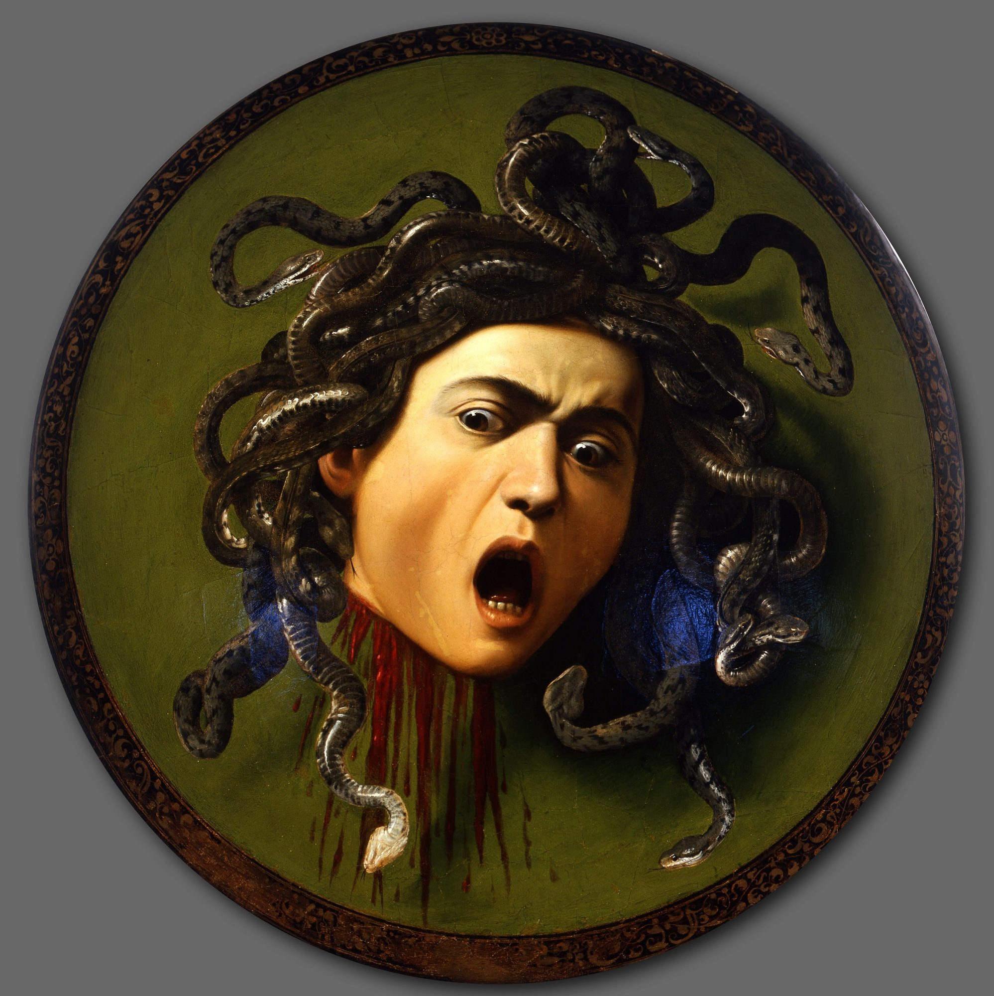 A severed, snake-haired head with wide staring eyes and mouth open in a scream, blood streaming from the neck, dark serpents writhing outward from the scalp against a green convex ground ringed by a gilt border — Caravaggio's Medusa, painted on a ceremonial parade shield, showing the Gorgon's face in the instant after decapitation.