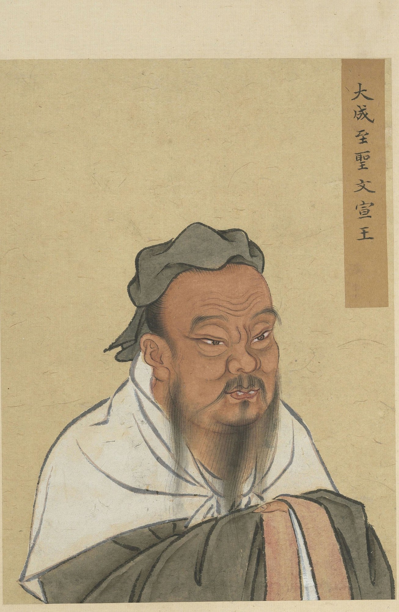 Half-length painted portrait of Confucius as an old man: a broad, deeply lined face with a long grey beard and drooping moustache, wearing a soft dark cloth cap and white inner robe under a grey outer robe, on aged tan silk, with a title cartouche of Chinese characters at upper right.