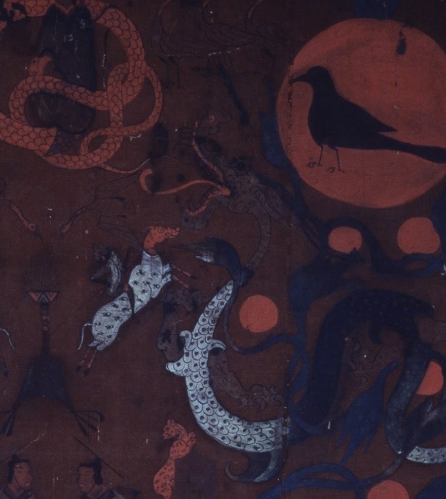 Detail from the upper 'heaven' register of the painted silk funerary banner from Mawangdui Tomb 1. A large red sun disc holds a black crow (the sun-crow), and below it several smaller red discs — the roosting suns — hang among the twisting dark-blue branches of the Fusang mulberry, with a coiled red serpent-bodied deity and dragons filling the field on the brown silk ground.