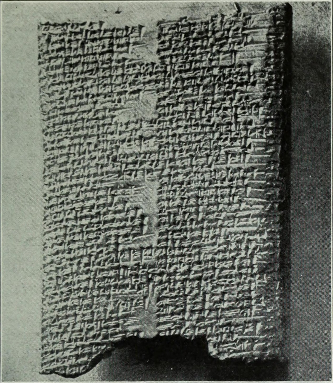 A photograph of the actual ancient clay tablet of the Fourth Tablet of the Babylonian Epic of Creation (Enūma Eliš), British Museum 93016: a broken rectangular fragment densely covered in columns of impressed cuneiform wedges, lit to cast a shadow on a plain ground.